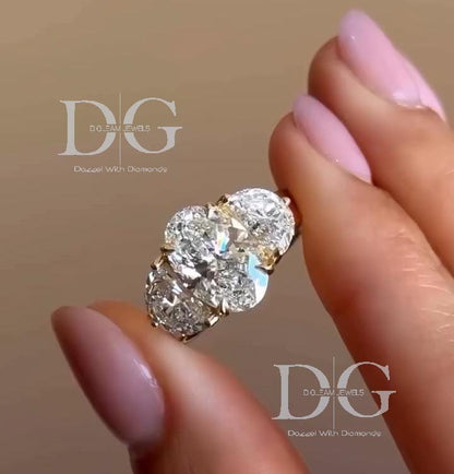 May include: A three-stone diamond ring with an oval-cut center stone and two side stones. The ring features a gold band and is held up to the light, showcasing the sparkle of the clear diamonds. The ring is a piece of jewelry, likely for engagement or special occasion.