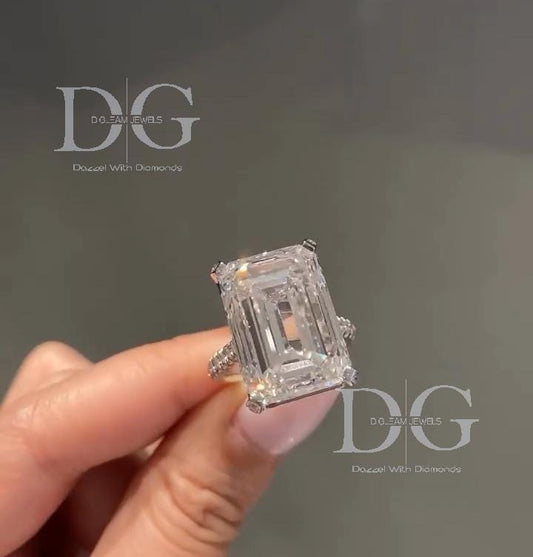 May include: An emerald-cut diamond ring. The large, rectangular diamond is the focal point, set on a band with smaller accent stones. The ring is held against a blurred background. The ring's setting appears to be platinum or white gold, enhancing the diamond's brilliance. The image includes the text 'D.O. EAM JEWELS' and 'Dazzle With Diamonds'.