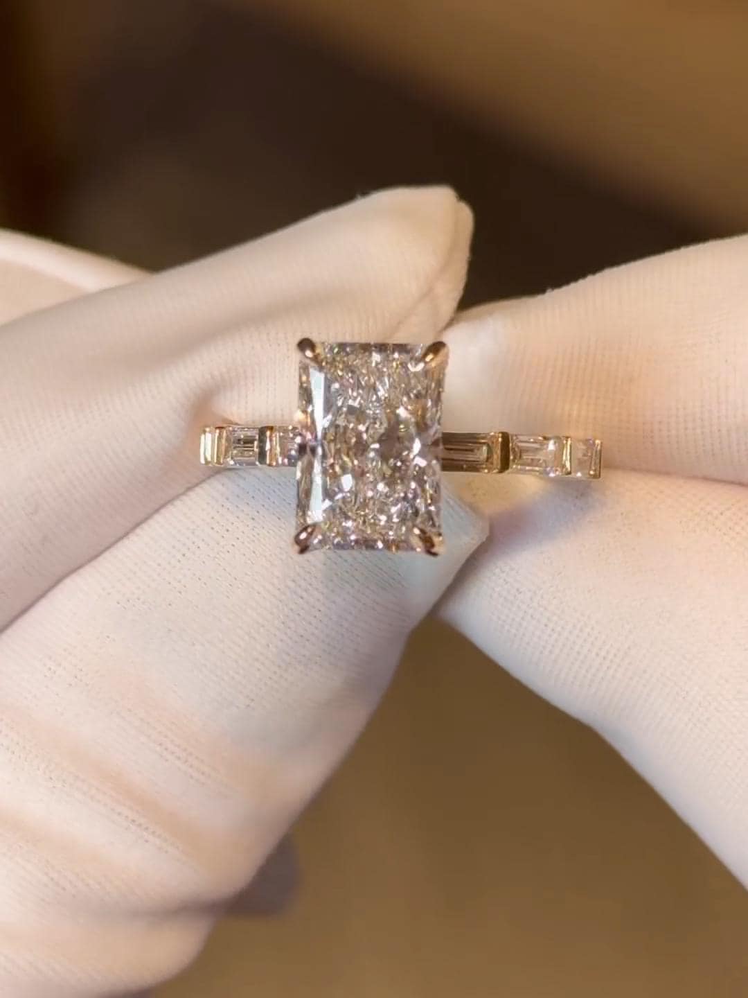 May include: A radiant-cut diamond engagement ring. The ring features a large, rectangular-shaped diamond as the center stone, with smaller baguette diamonds on either side of the main stone and on the band. The setting appears to be rose gold, with a delicate and elegant design, showcasing the brilliance of the diamonds.
