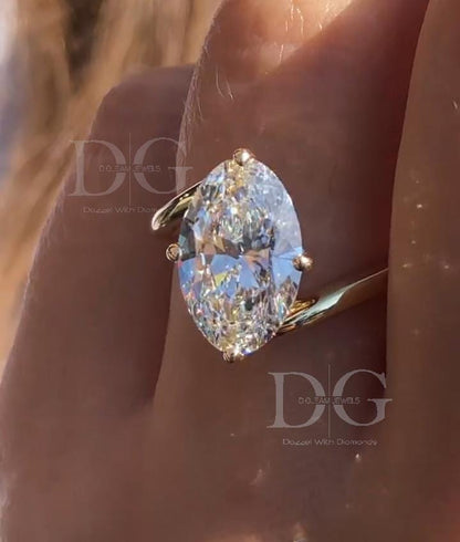 May include: A marquise-cut diamond ring with a gold band. The diamond is large and clear, with multiple facets reflecting light. The ring's band is a simple, polished gold, and the diamond is held in place by four prongs.