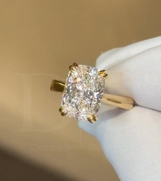 May include: A radiant-cut diamond engagement ring. The ring features a large, rectangular-shaped diamond with a brilliant, clear appearance. The diamond is set in a gold band with four-prong settings. The ring is displayed against a white background.